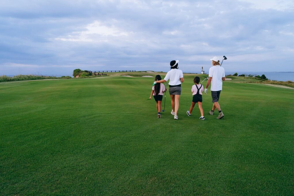 Family walking a lush golf course carrying junior golf clubs