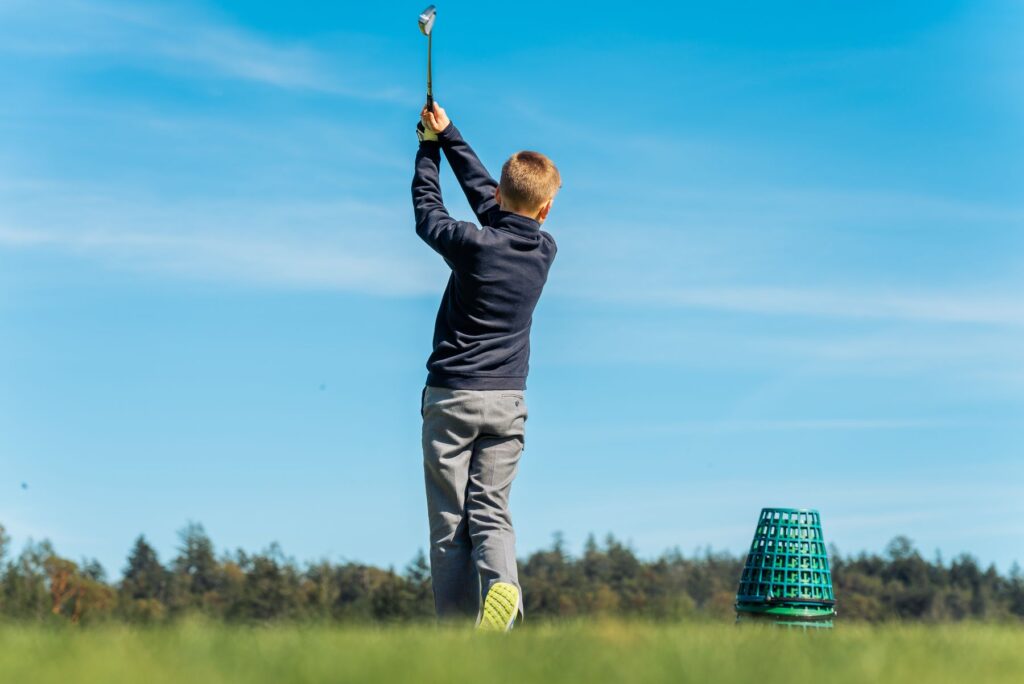 Young boy practicing his golf swing outdoors on a bright day