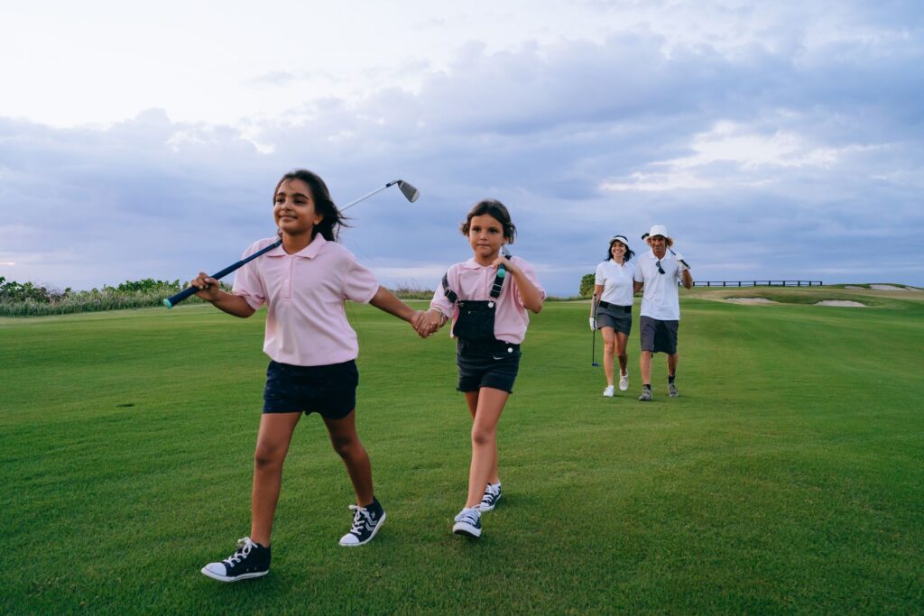 Two siblings holding hands while carrying a junior golf club